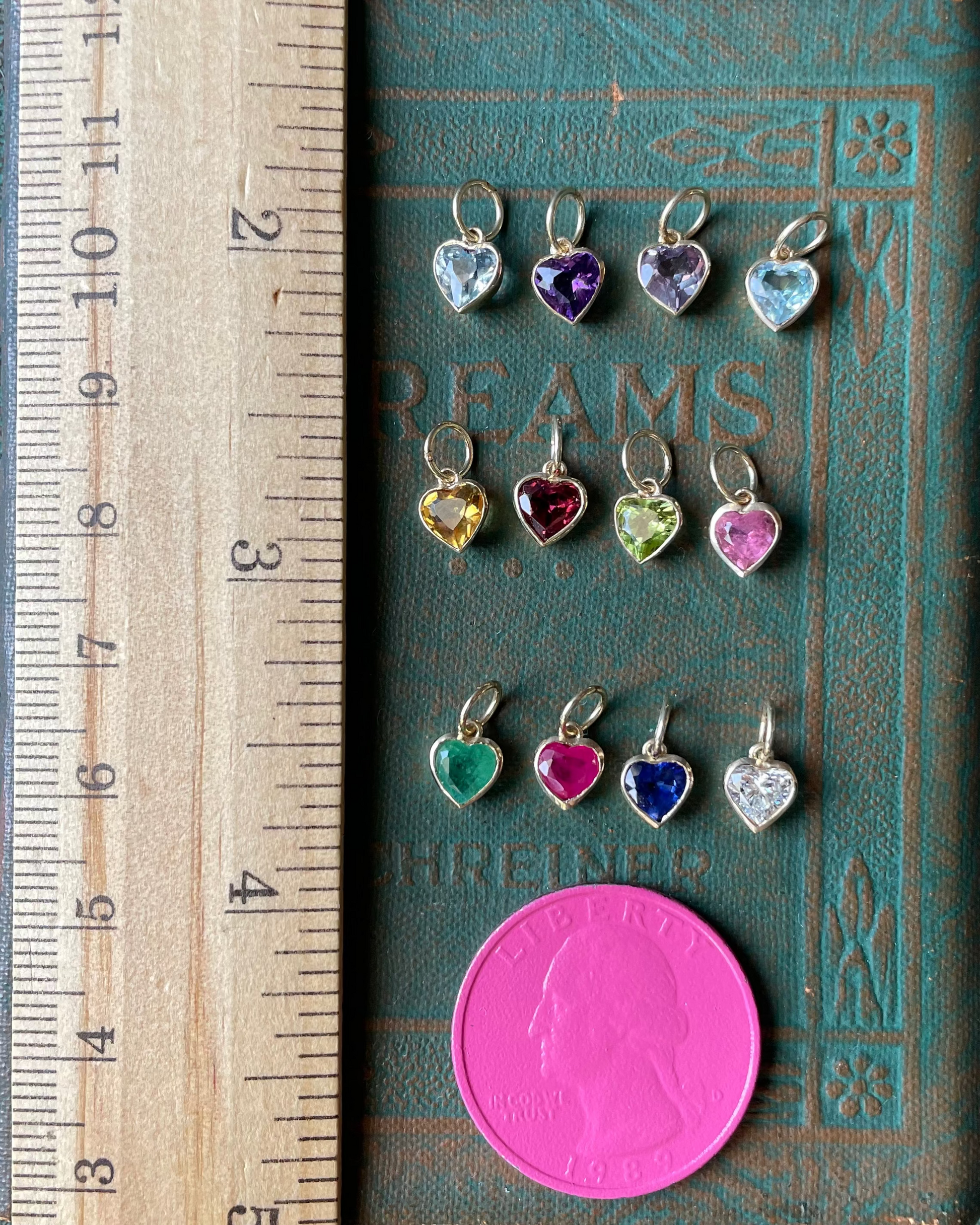 Heart-shaped charms with colored stones on a book next to a ruler for scale.